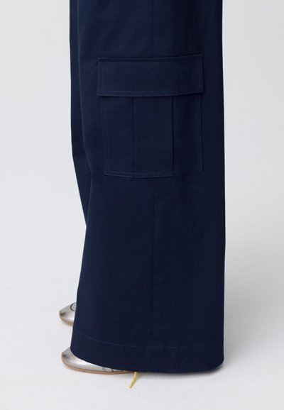 Pantalones cargo en color azul marino con pierna amplia, que cuentan con un bolsillo lateral, tejido de algodón suave y costuras en contraste.
