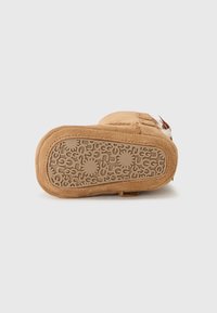 Tan mockasiner i mocka med en texturerad gummisula som har ett cirkulärt mönster och en liten logotags på sidan.