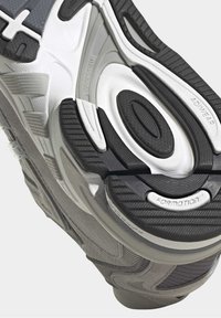 Shoe sole featuring gray, black, and white materials. Textured rubber, smooth sections, and flex grooves for enhanced grip and support.