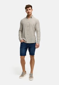 Camicia a maniche lunghe con righe verticali beige e navy, abbinata a pantaloni corti di jeans scuri e sneaker grigie chiare. Fit casual.