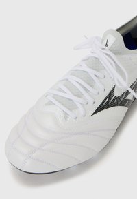 Witte sportieve schoen met een gestructureerde leren bovenkant, afgewerkt met gestikte accenten en zwarte branding, aangevuld met witte veters en een grijze tong.