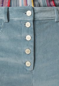 Helleblaue Cordhosen mit vertikalen Rippen, einer Fünf-Knopf-Front und gesteppten Akzenten entlang des Bundes und der Taschen.