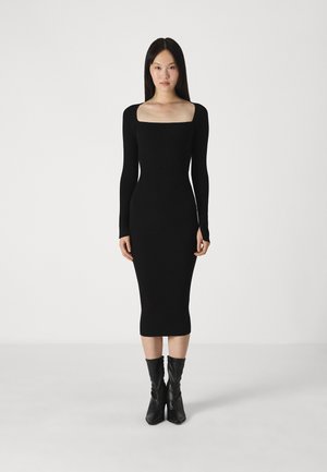 Robe noire à côtes avec des manches longues, décolleté carré et une silhouette ajustée, s'étendant jusqu'au mollet. Assortie avec des bottes noires arrivant aux genoux.