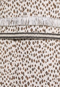 Tissu avec un fond beige parsemé de taches léopard marron et noires, accentué par des bords frangés et une décoration noire.