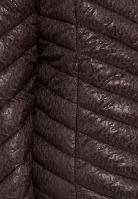 Veste matelassée marron avec un motif en damier, présentant une texture brillante et un design de logo répété dans des teintes sombres, des zips et une forme épurée.