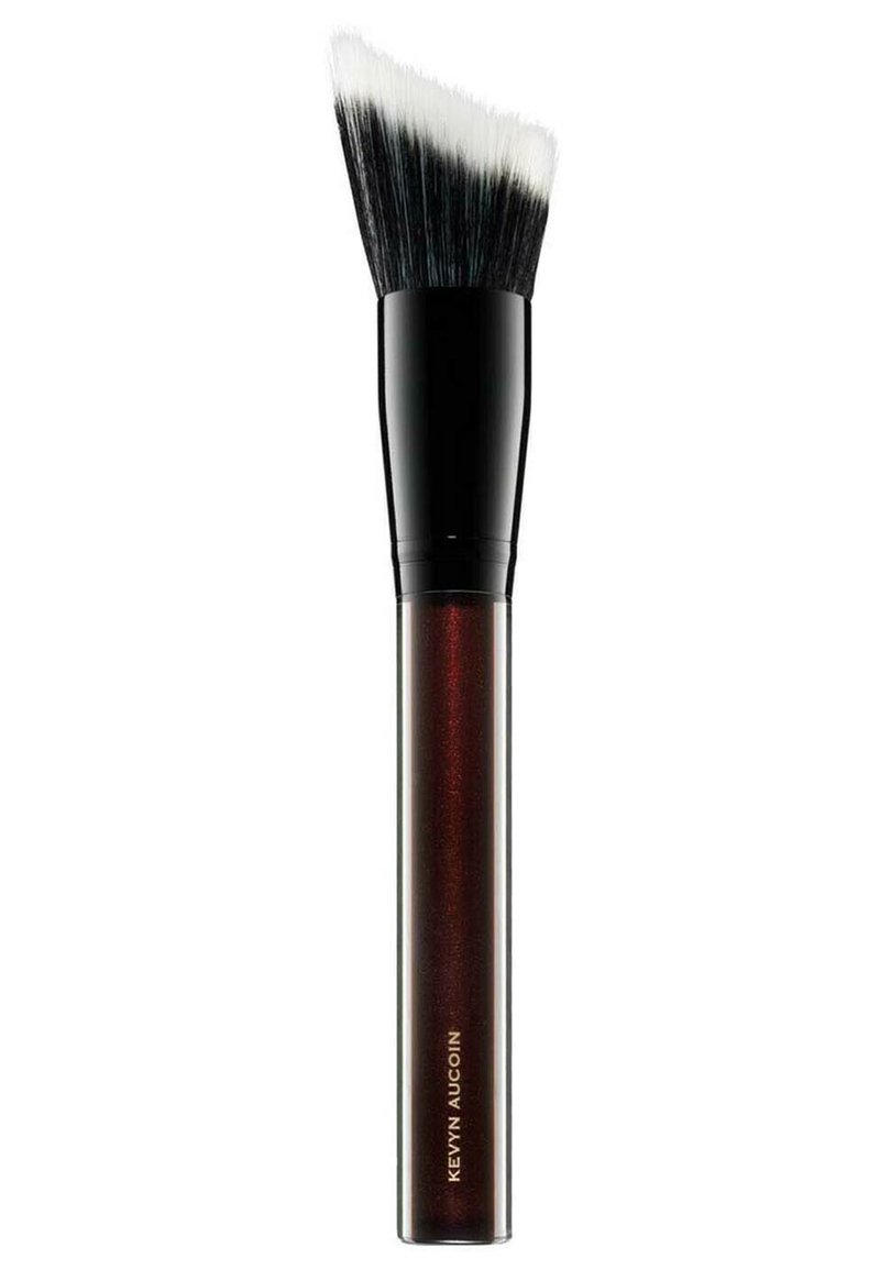 Pennello per trucco con una testa piatta e inclinata, dotato di setole nere e un manico lucido di un rosso scuro con testo dorato che recita "Kevyn Aucoin."