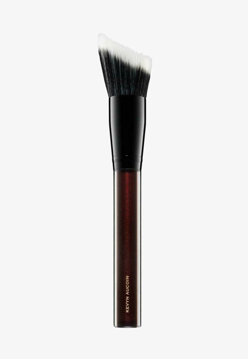 Pennello per trucco con una testa piatta e inclinata, dotato di setole nere e un manico lucido di un rosso scuro con testo dorato che recita "Kevyn Aucoin."