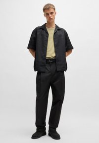 Chemise noire à manches courtes avec un motif subtil, superposée sur un T-shirt vert clair. Associée à un pantalon noir et des chaussures noires texturées.