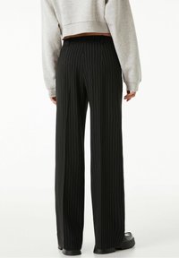 Svarta randiga vida byxor med en tjock midjeband, som har en mjuk textur och en ren, skräddarsydd passform. Kompletteras av svarta skor.