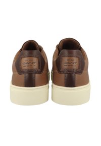 Baskets en cuir marron avec un accent contrasté marron foncé sur le talon, semelle en caoutchouc crème et logo de la marque à l'arrière. Surface texturée.