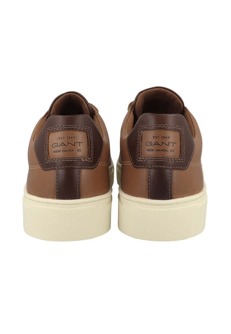 Zapatillas de cuero marrón con un acento en un marrón oscuro en el talón, suela de goma color crema y logo de la marca en la parte trasera. Superficie texturizada.