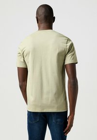 Oliwkowa bawełniana koszulka z krótkim rękawem i okrągłym dekoltem. Gładka faktura, minimalistyczny design, noszona z ciemnoniebieskimi dżinsami.