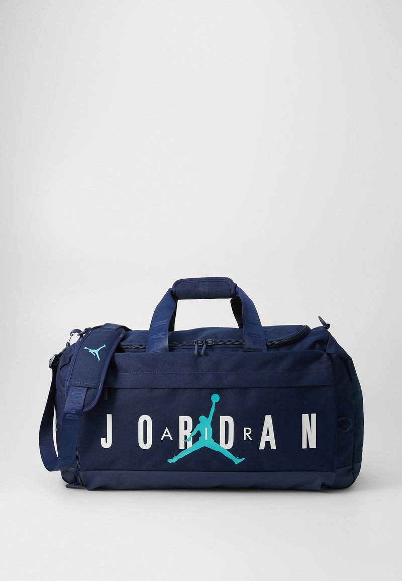 Mornarska torba z dvignimi ročaji v beli barvi "JORDAN" in teal Jumpman logotipom. Ima dvojne ročaje, nastavljiv trak in zadrževalni predal. Izdelana iz trpežnega materiala.