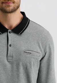 Graues Polohemd mit schwarzem Kragen, das mit einem strukturierten Muster und einer Brusttasche versehen ist. Zweiknopf-Leiste mit Kontrastnähten.