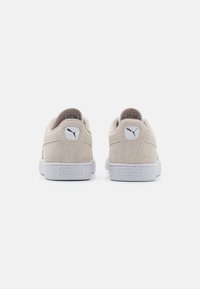 Baskets en daim beige avec semelles en caoutchouc blanches, comportant un logo rond sur le talon et "PUMA" embossé sur le côté, design minimaliste.