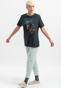 T-shirt nera in cotone con stampa grafica colorata; abbinata a pantaloni a sigaretta verde menta, caratterizzati da una texture morbida e orlo alla caviglia.