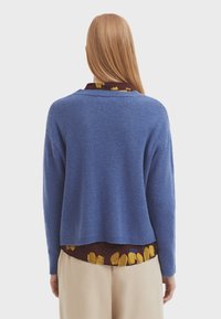 Blå stickad tröja med en lös passform och sänkta axlar, med en ribbad nederkant och strukturerad tyg. Lagerlagd över en mönstrad blus.