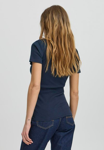 Tricou ajustat de culoare albastru marin, cu mâneci scurte, textură ribbed și decolteu rotund, asortat cu blugi închis la culoare.