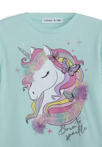 T-shirt in cotone azzurro chiaro con grafica di un unicorno dai capelli pastello, dettagli in argento, farfalle e testo "Nato per brillare".