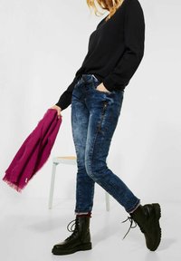Vaqueros de mezclilla en lavado oscuro con un ajuste slim, que cuentan con bolsillos con cremallera y costuras en contraste. Combinados con una camiseta negra y botas de combate negras.