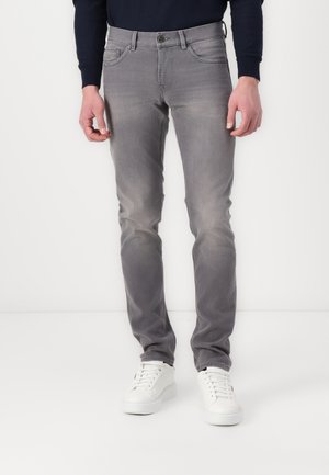 Graue Denim-Jeans im Slim-Fit-Stil, mit Knopfverschluss, fünf Taschen und subtiler Ausbleichung. Kombiniert mit weißen Sneakers.