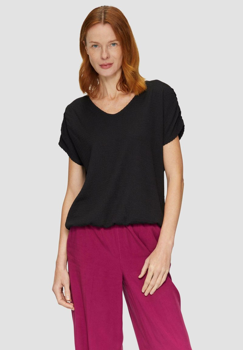 Zwarte blouse met textuur, een V-hals en opgerolde korte mouwen, gecombineerd met felmagenta, loszittende broeken. Soepele stof, casual ontwerp.