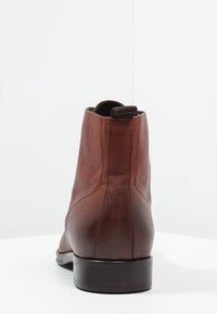 Stivale alla caviglia in pelle marrone con una texture liscia, linguetta superiore e un design elegante. Suola piatta in gomma e dettagli di cucitura minimi.