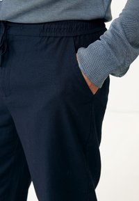 Laivastonsiniset housut, joissa on joustava vyötärönauha ja kiristysnyöri, sivutaskuilla ja sileällä pinnalla, osittain näkyvissä harmaan paidan kanssa.