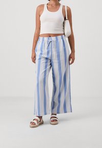 Blå och vita randiga vida byxor med dragsko i midjan, som bärs tillsammans med en vit ribbad linne och avslappnade vita sandaler.