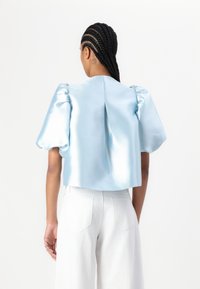 Lys blå satin cropped bluse med puffede ærmer, med en centralt bagsidefald. Båret med hvide brede bukser. Glat tekstur.