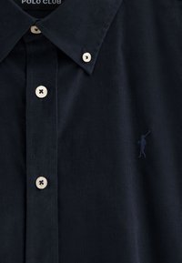 Camicia in corduroy blu navy con colletto classico, chiusura frontale con bottoni chiari e logo tono su tono ricamato sul petto.