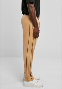 Lichtbeige fluwelen broek met zwarte zijstrepen, voorzien van zijzakken en een elastische tailleband, gedragen met witte sneakers.