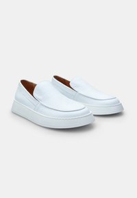 Baltas ādas slip-on kurpes ar noapaļotu purngali, teksturētu augšdaļu un biezu zoli. Gluda apdare ar smalku adījuma detaļu.