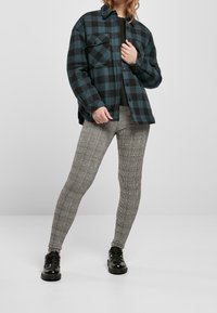 Camisa de franela a cuadros en verde oscuro y negro, con dos bolsillos en el pecho. Combinada con leggings a rayas ajustados en tonos neutros y zapatos negros.