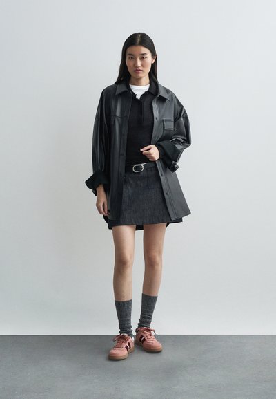 Svart skinn oversized skjortejakke over en svart topp, parret med en grå denimskjørt. Rosa sneakers med mørke aksenter og grå strikkede sokker.