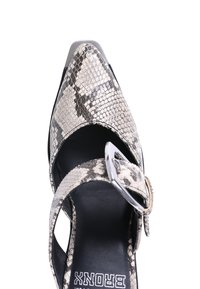 Pantofii cu toc înalt și vârful ascuțit, cu un model de piele de șarpe. Au un interior negru, curea ajustabilă cu cataramă argintie și un capac metallic pentru toc.