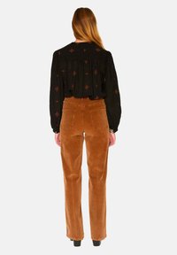 Pantalons en velours côtelé marron taille haute avec des jambes droites, deux poches arrière et une surface texturée. Associés à un blouse noire brodée.