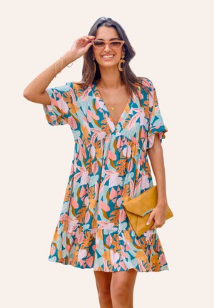 Korte mouwen, V-hals jurk in teal met levendige bloemen- en bladerenpatronen in roze, oranje en groen. Heeft een gelaagde rok en een gele clutch.