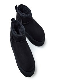 Botines de ante negro con forro suave, punta redonda y suela de goma. Presentan una costura acolchada y una lengüeta para facilitar su puesta.