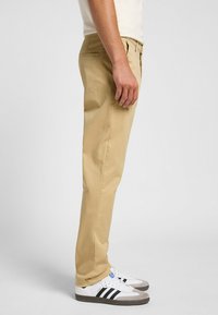Chinos de algodón beige con un corte ajustado, bolsillos delanteros y un bolsillo trasero, combinados con zapatillas blancas con rayas negras.