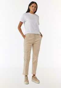 Witte t-shirt met korte mouwen met de tekst "VOILA", gecombineerd met kaki cargobroek met zijzakken, en beige sneakers met een gestructureerde zool.