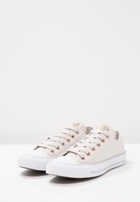 Canvas-sneakers med ljusbeige ovandel, vit gummisula, snördesign med metallöglor och kontrasterande vit tåkappa.