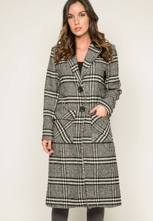 Manteau à carreaux long en noir et blanc. Fabriqué en tissu texturé avec de grandes poches et un devant à double boutonnage. Détail de col à revers notable.