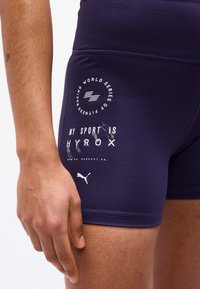 Κοντινό πλάνο στο μηρό ενός ατόμου που φοράει σκούρο μπλε αθλητικό σορτς με λευκό κείμενο και λογότυπα, συμπεριλαμβανομένων των λέξεων "My Sport is Hyrox" και του λογότυπου Puma.