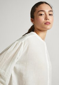 Camicia bianca, leggera, con bottoni, dalla consistenza morbida, caratterizzata da maniche arricciate, colletto e una vestibilità rilassata. Tessuto con una leggera lucentezza.