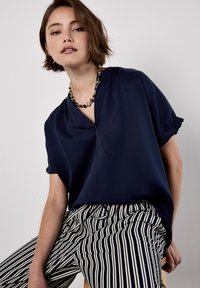 Top navy a maniche corte con scollo a V e leggera arricciatura sulle maniche, abbinato a pantaloni a righe navy e bianchi con una vestibilità rilassata.