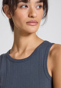 Gray ribbed tank top featuring a round neckline and wide armholes, made from a soft textured fabric with vertical stripes.