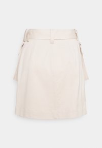 Krémová sukně ke kolenům s vysokým pasem, poutek na opasek a bočními kapsami s klopou, vystavená na jednobarevném pozadí.