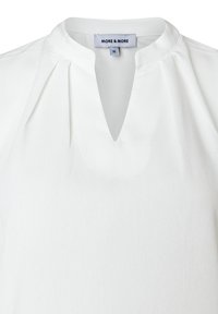 Weiße Bluse mit runder Halslinie und einem kleinen V-Ausschnitt, ausgestattet mit Falten nahe dem Kragen und einem sichtbaren Markenetikett im Kragen.