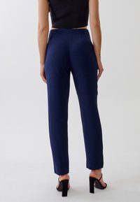 Tmavě modré kalhoty s vysokým pasem vyrobené z hladké látky, s přizpůsobeným střihem, čistými liniemi a minimalistickým designem.